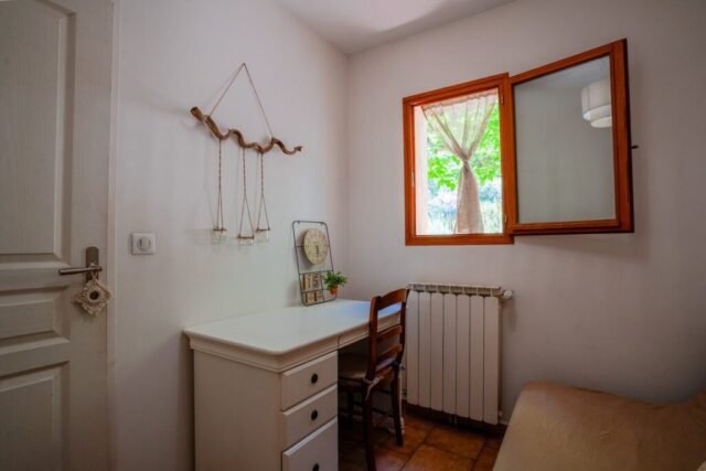 Chambre d'appoint avec bureau, chaise et commode, éclairée par une fenêtre côté jardin Chambre d'appoint avec bureau, chaise et commode, éclairée par une fenêtre côté jardin