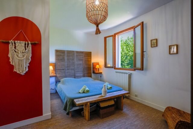Chambre double au mur terracotta, lit king size, macramé et fenêtre ouverte sur la verdure Chambre double au mur terracotta, lit king size, macramé et fenêtre ouverte sur la verdure