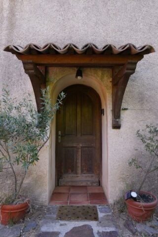 Porte d'entrée en bois du mas sous son auvent de tuiles, encadrée de pots en terre cuite Porte d'entrée en bois du mas sous son auvent de tuiles, encadrée de pots en terre cuite